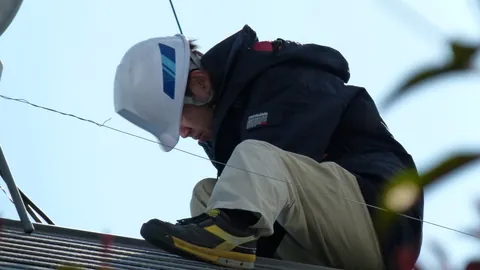 Operario con casco trabajando agachado sobre una cubierta durante una instalación solar