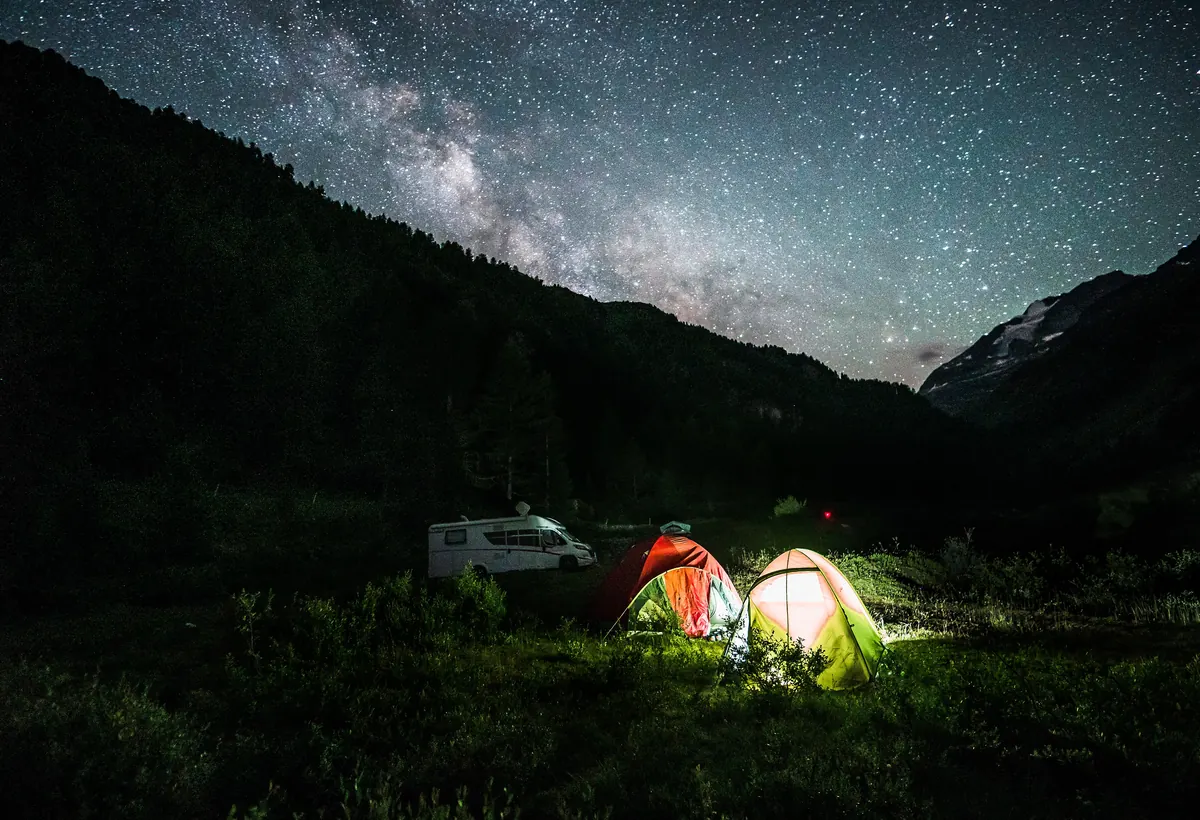 Tiendas de campaña iluminadas por dentro bajo la Vía Láctea, en alta montaña